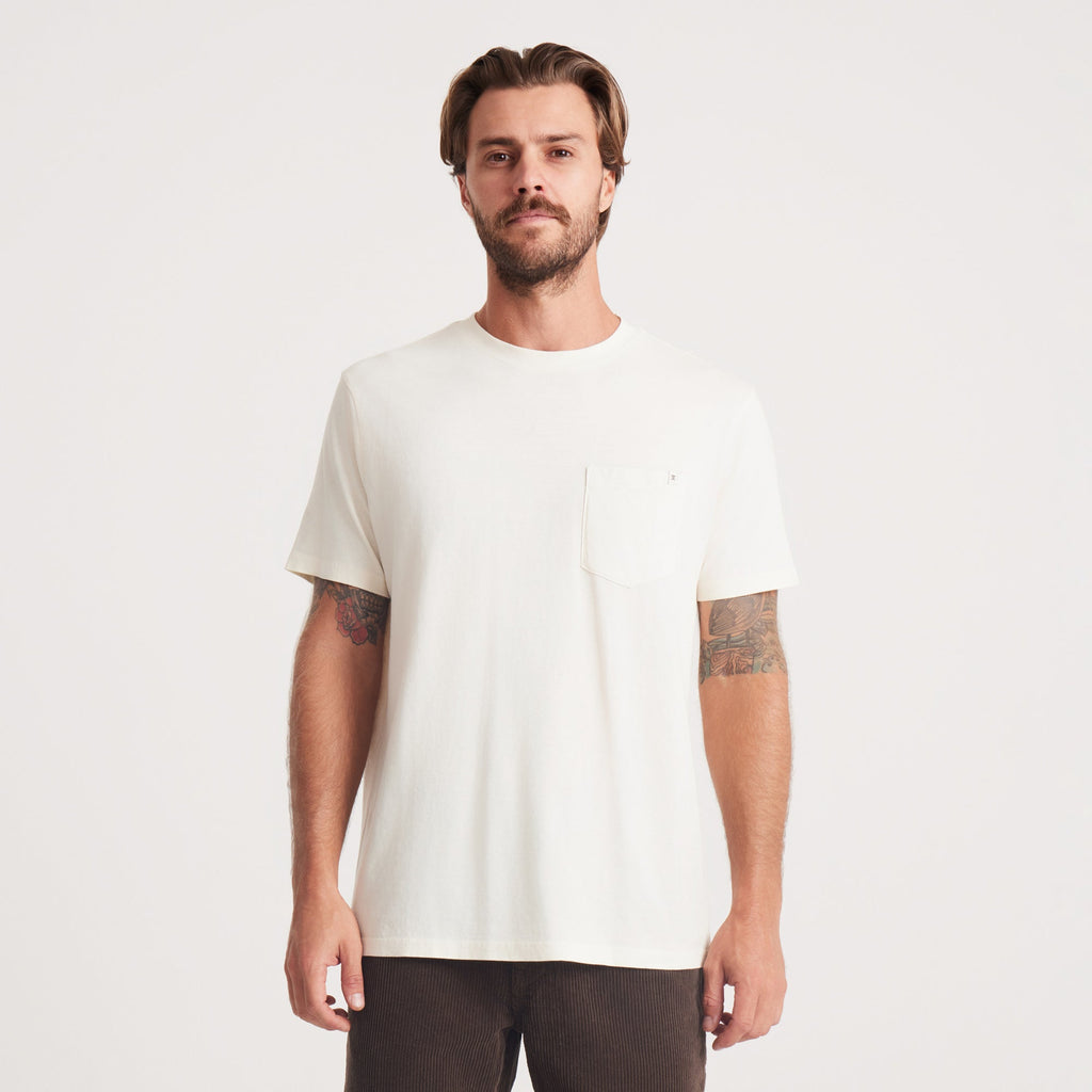 A man stands confidently wearing a white Roark t-shirt, featuring a pocket on the left side, showcasing casual style and comfort. Big Image - 3