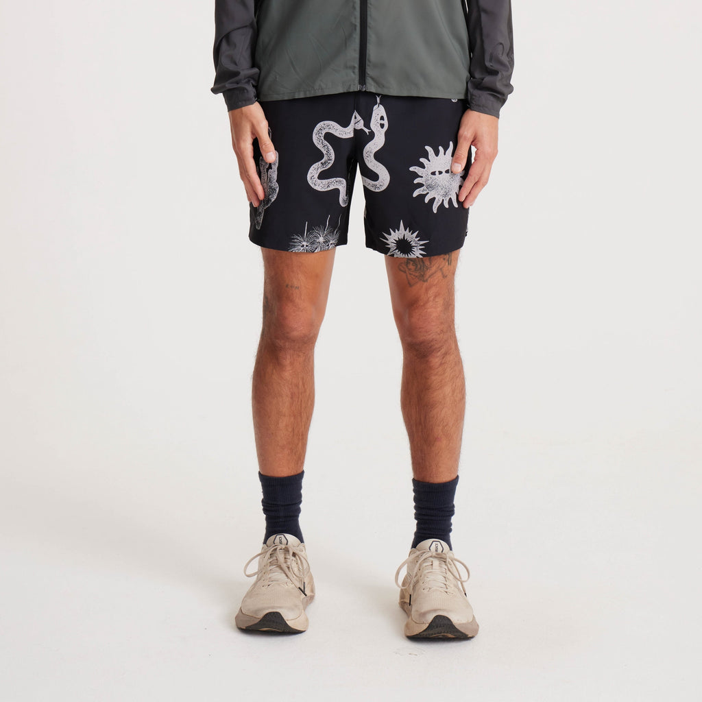 Model wearing black swim shorts with white graphic prints of snakes and desert-inspired patterns, styled with a lightweight jacket and sneakers for a casual summer look. Big Image - 2