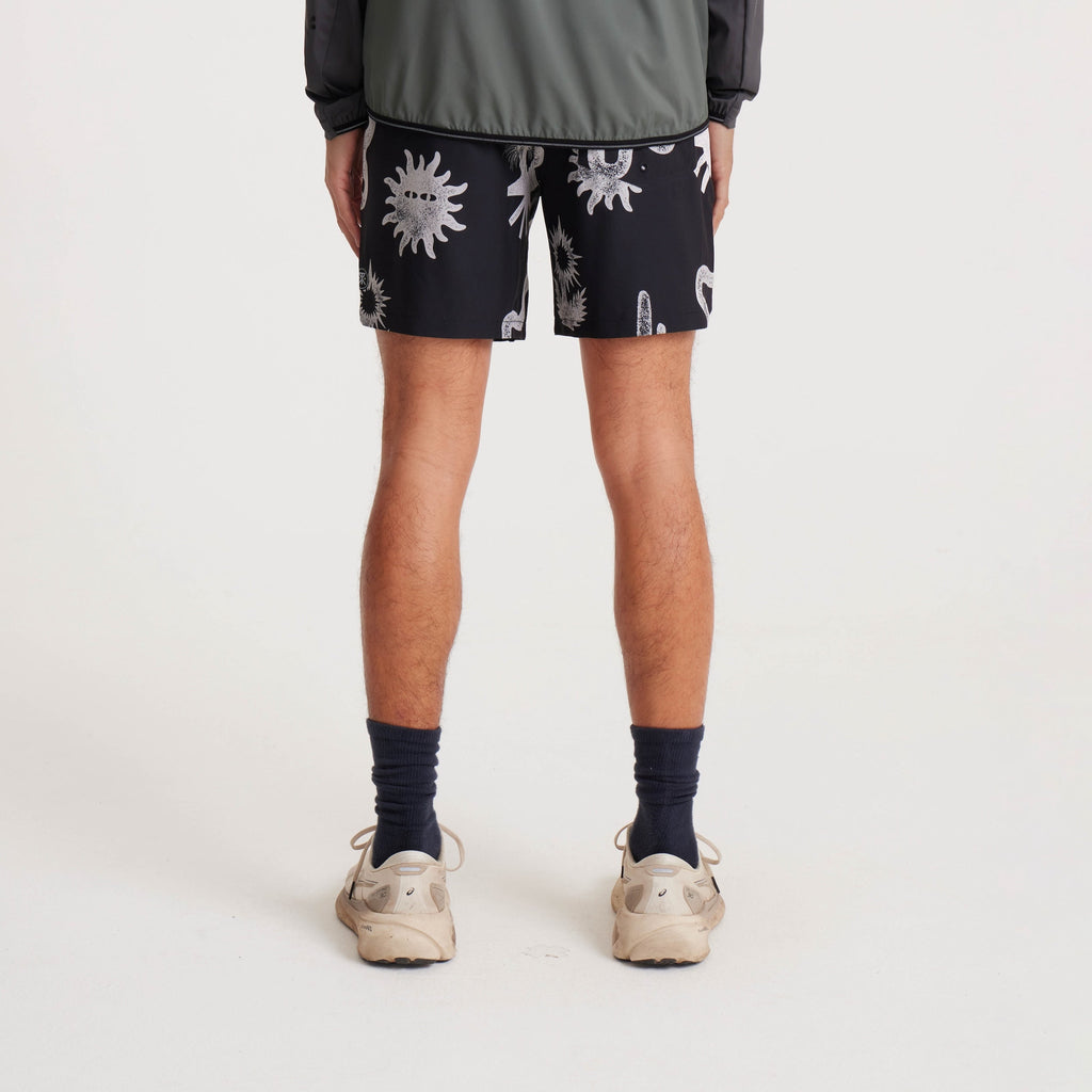 Back view of black swim shorts featuring white graphic desert-inspired designs, including snakes and abstract suns, paired with a casual jacket and sneakers. Big Image - 5