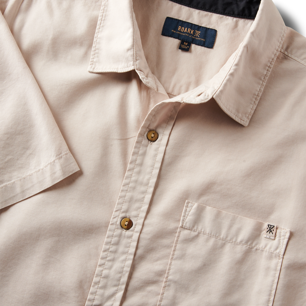 Close-up of the Roark Made To Fade Short Sleeve Button Up Shirt's collar, buttons, and chest pocket with embroidered logo in Washed Bone. Big Image - 9