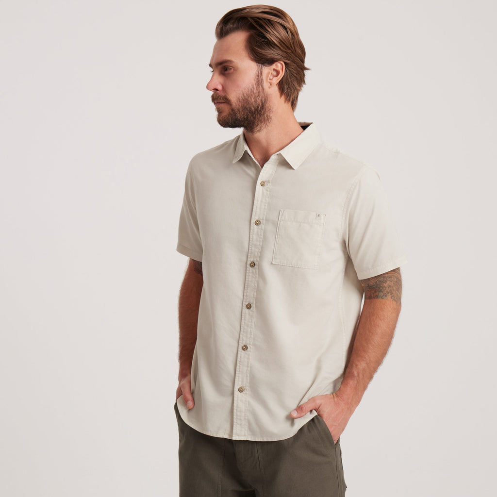 Side profile of a man wearing an off-white short-sleeve button-down shirt, showcasing a comfortable fit and modern styling. Big Image - 6