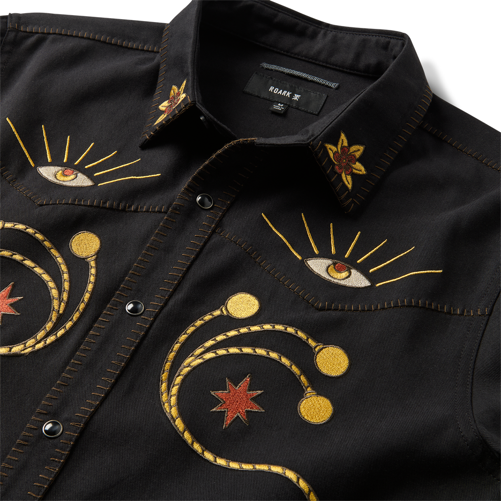 Close-up detail of a black denim Roark adventure jacket featuring rugged buttons, sturdy collar, and practical pockets, designed for travel and outdoor activities. Big Image - 11