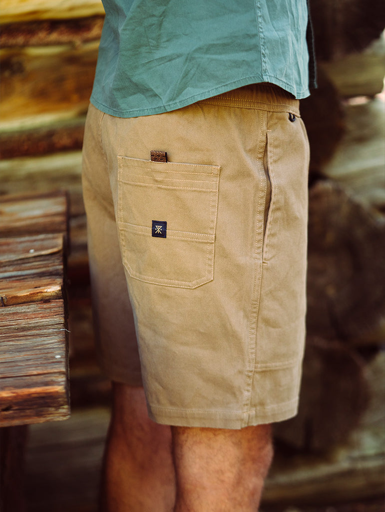 Person wearing beige shorts with a brand logo in front of a wooden background Big Image - 2