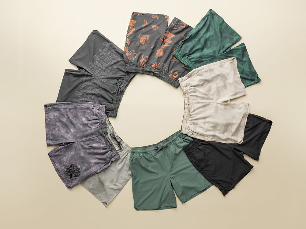 Collection of men's sun and workout shorts in various colors arranged in a circular pattern on a beige background.
