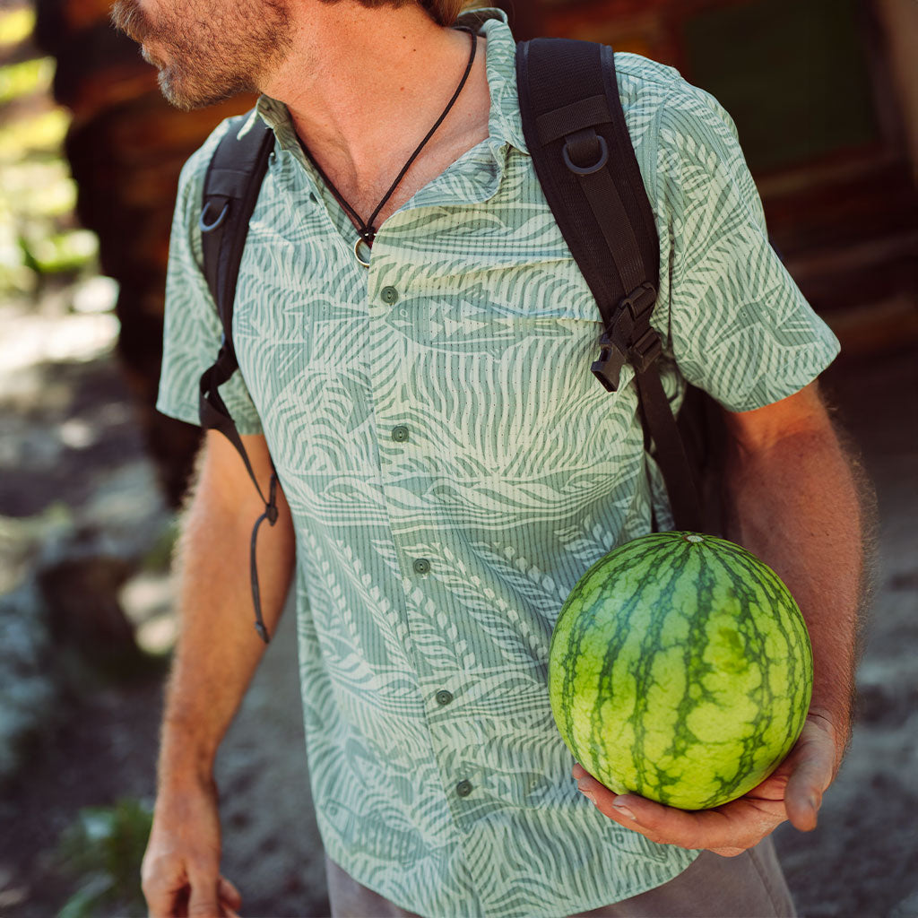 Man in a lightweight, fish pattern shirt, holding a watermelon outdoors with a blurred background Big Image - 2