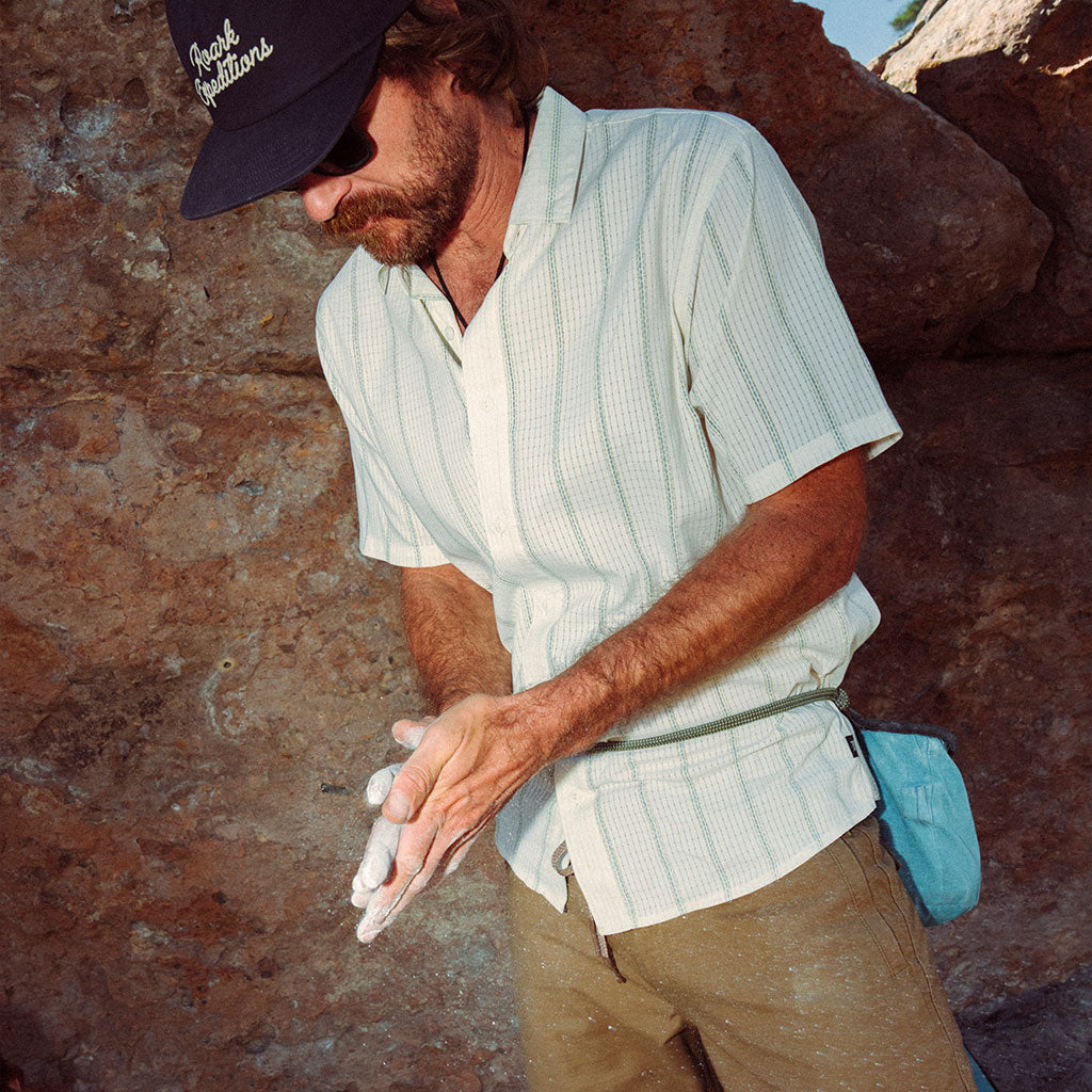Man in outdoor setting wearing a cap and light shirt, standing against a rock wall. Big Image - 2