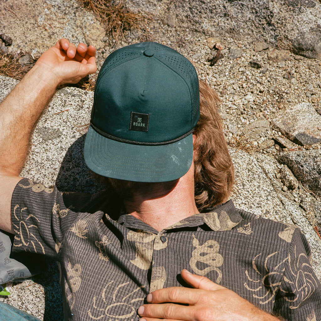 Person wearing a green cap and patterned shirt sitting on rocks Big Image - 2