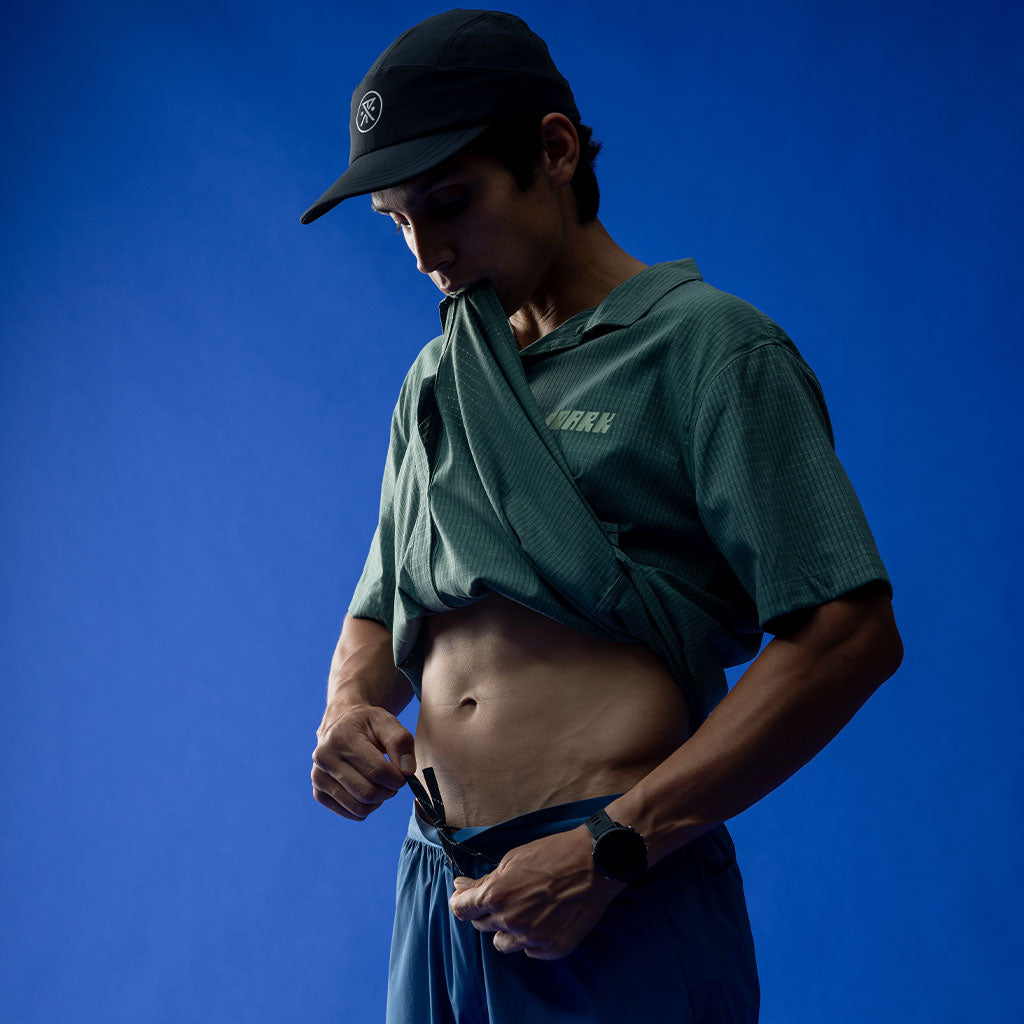 Man wearing a green shirt and blue shorts against a blue background Big Image - 2