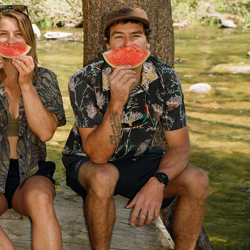 Two people sitting by a river, eating watermelon slices. Big Image - 2